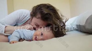 美丽的卷曲女人亲吻和拥抱一个一岁的孩子。 妈妈和孩子<strong>挠痒痒</strong>，笑